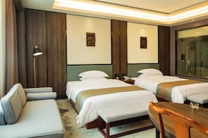A hotel room with two beds, a sofa, a wooden table, and a large mirror.