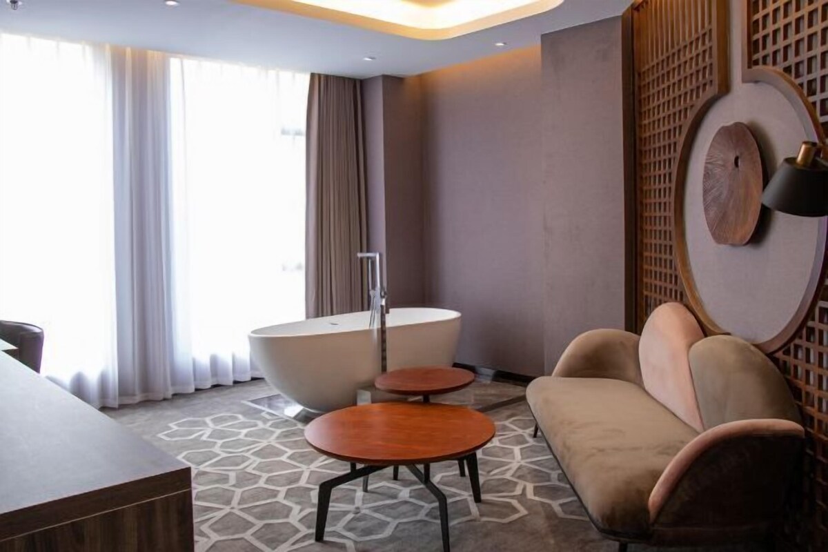 A modern room with a bathtub, a sofa, a small table, and a desk.