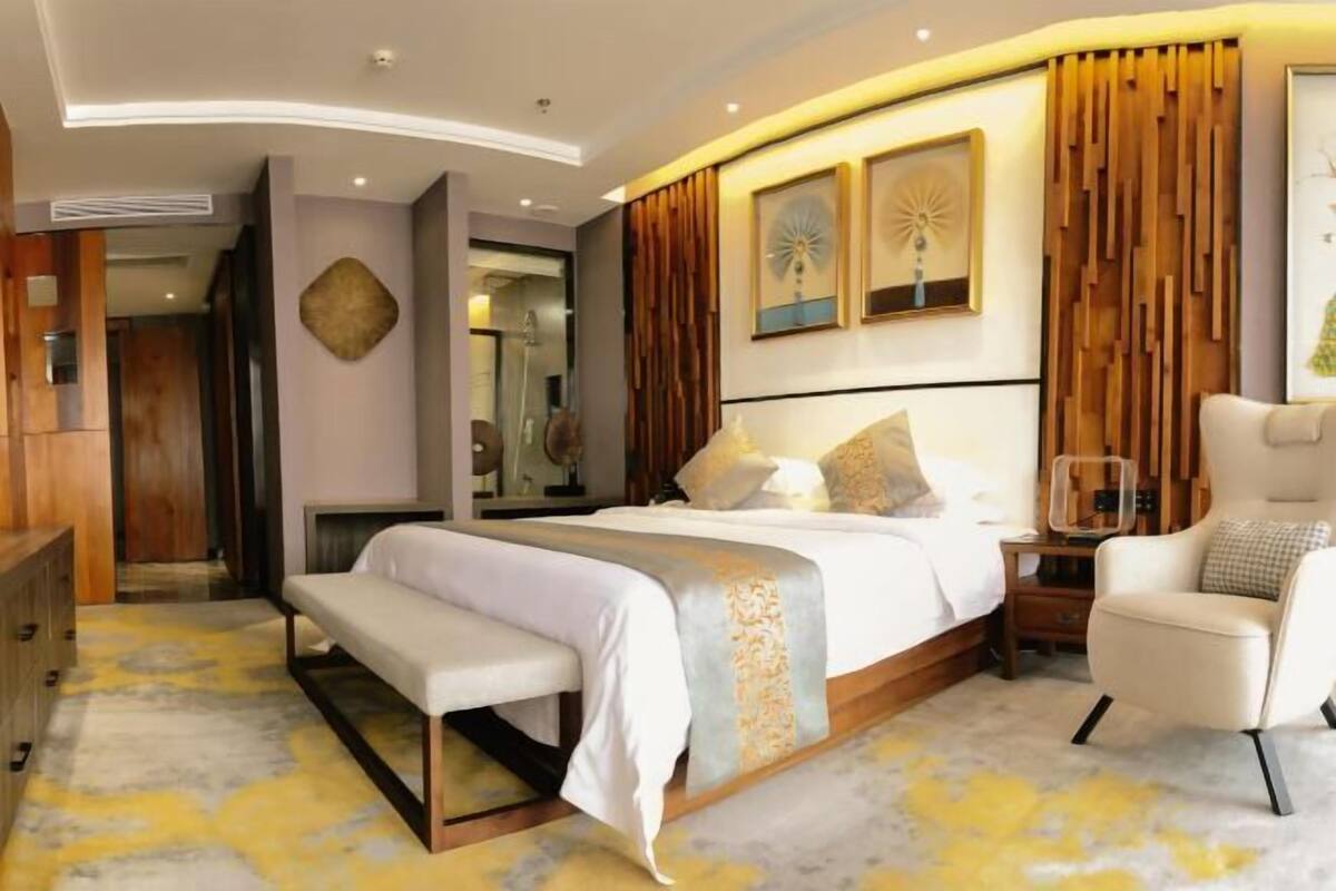 Un dormitorio moderno con cama, banqueta, silla y una obra de arte en la pared.