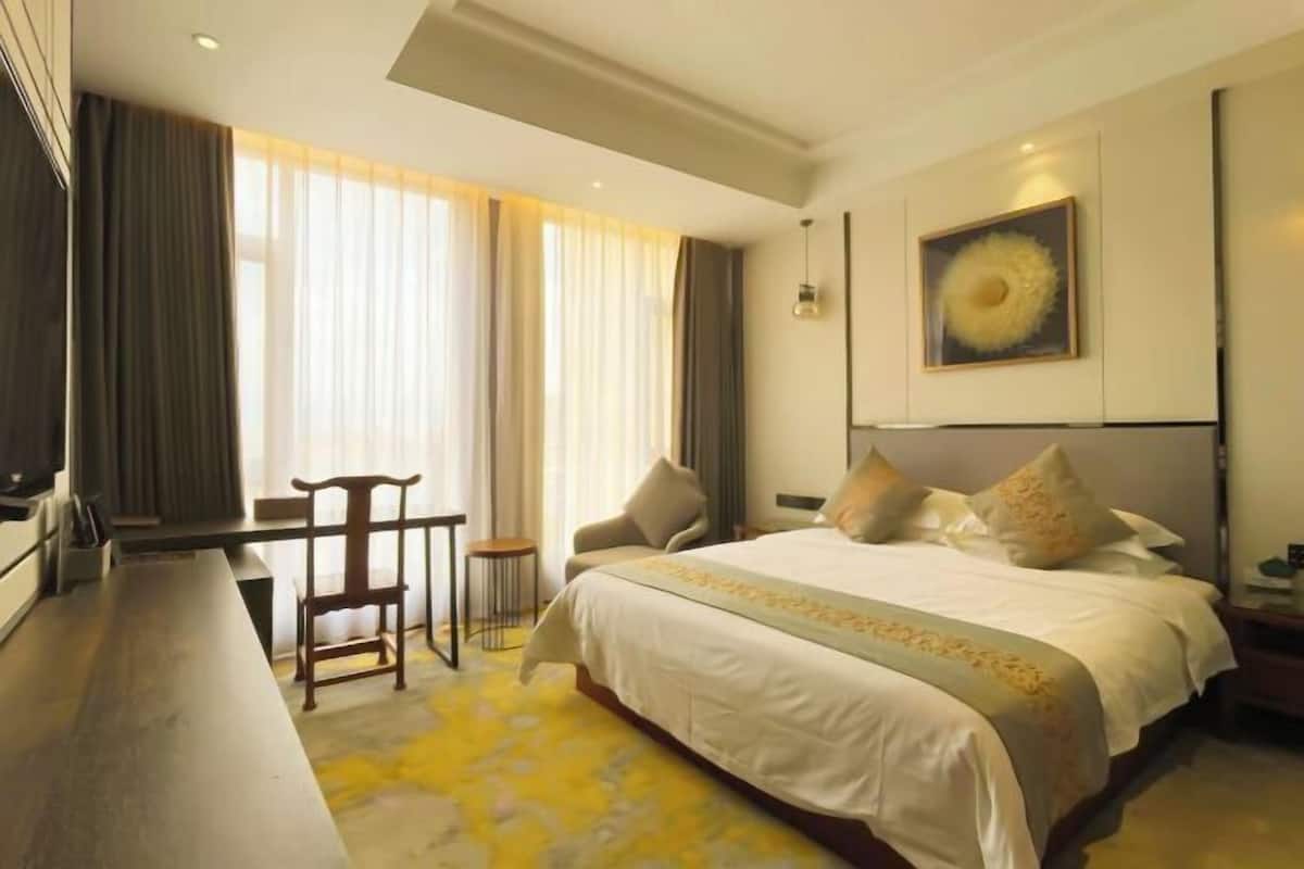 Una habitación de hotel con una cama grande, un escritorio con silla, televisión y un ventanal con cortinas.