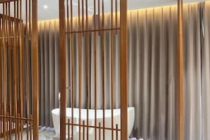 A modern bathroom with a large bathtub, vertical wooden slats, and a neutral color scheme.
