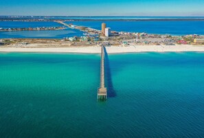 An aerial view of a coastal area with a prominent pier extending into the turquoise waters.