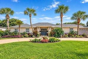 A residential house with a front lawn, palm trees, and a driveway.