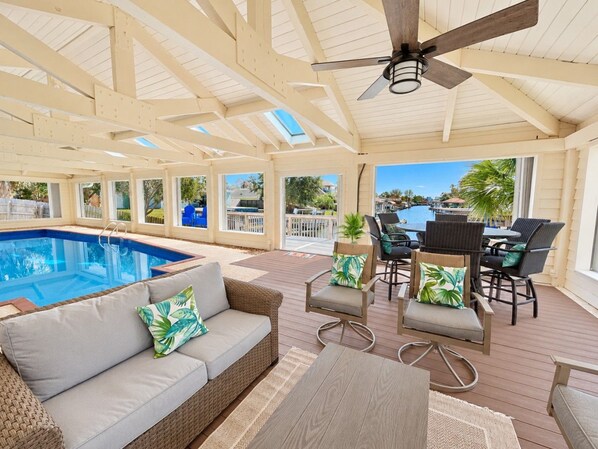 An indoor pool area with a ceiling fan, a pool, and seating arrangements.