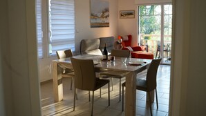 A dining area with a table set for four, a sofa, and a painting on the wall. - Beautiful apartment 50m from the marina (Saint-Valery-sur-Somme)