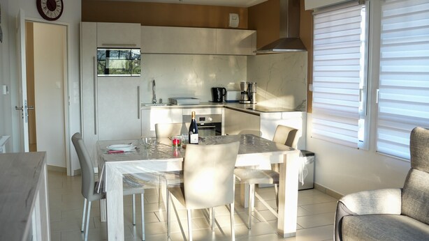 A modern kitchen with a dining area, featuring a built-in oven, a coffee maker, and a window with blinds. - Beautiful apartment 50m from the marina (Saint-Valery-sur-Somme)