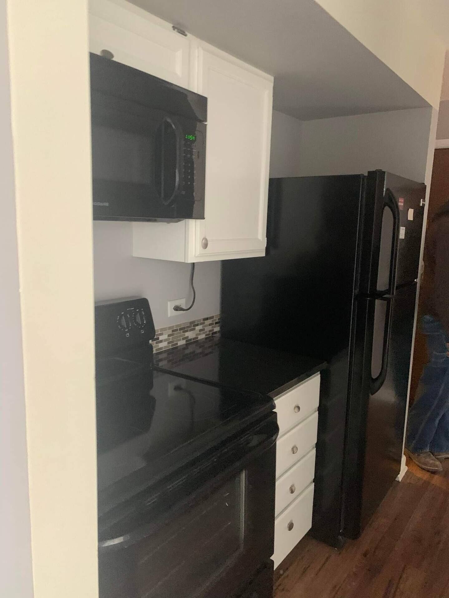 Eine kleine Küche mit einer schwarzen Mikrowelle, einem schwarzen Kühlschrank und einem weißen Schrank.