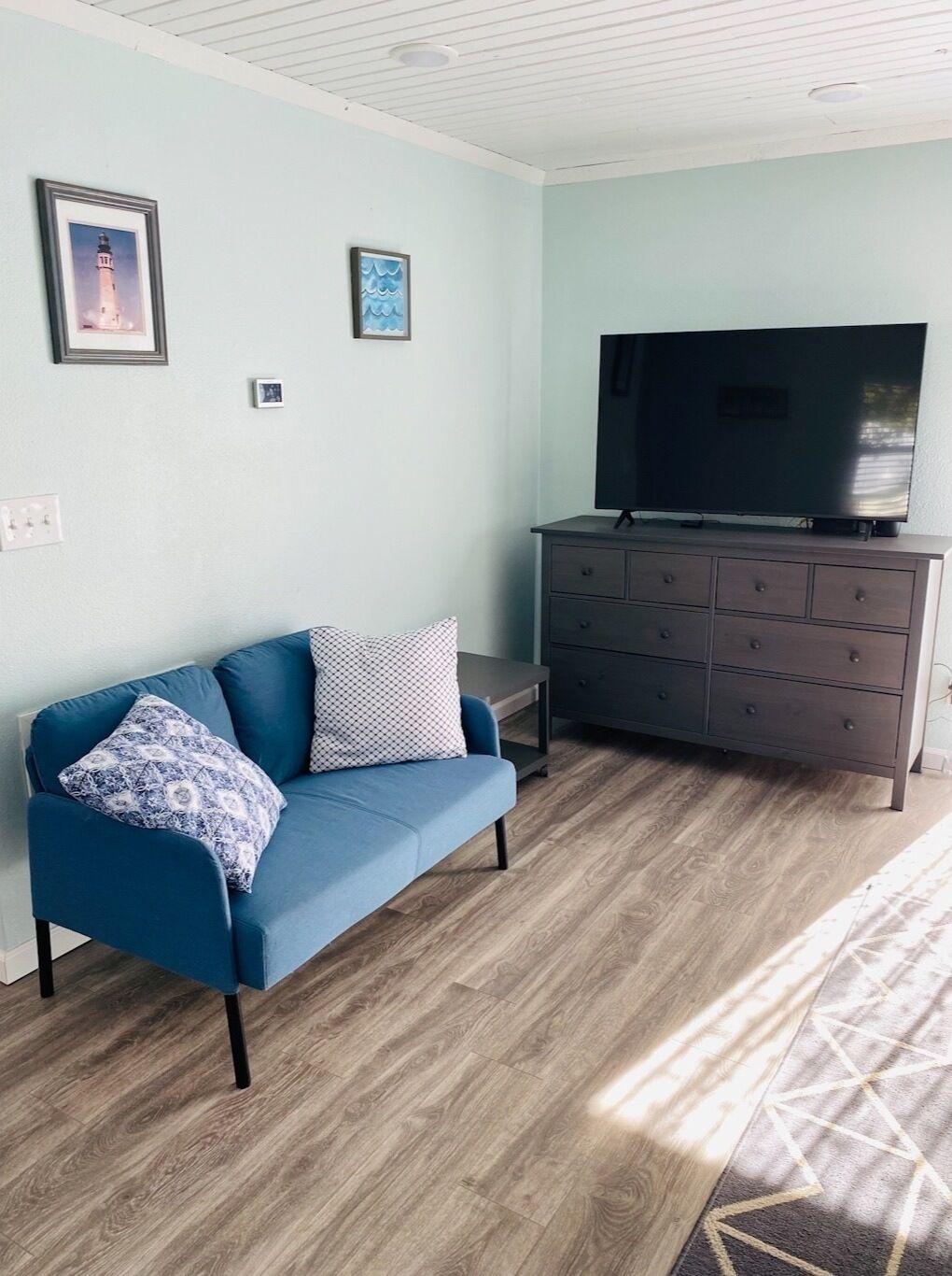 Ein Wohnzimmer mit einem blauen Sofa, einer dunkelholznen Kommode und einem Flachbildfernseher.