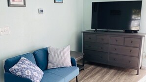 Een woonkamer met een blauwe bank, een donker houten dressoir en een flatscreen televisie.