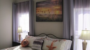 Une chambre à coucher avec un lit, deux lampes de chevet, un tableau accroché au mur et des rideaux.
