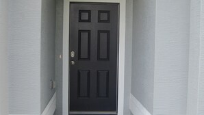 Une porte noire avec un paillasson sur lequel on peut lire : « C’est bon de rentrer à la maison. »
