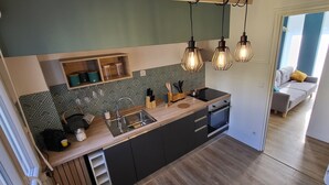 Eine moderne Küche mit Holzarbeitsplatte, schwarzen Schränken und einem eingebauten Backofen. Hängelampen und eine Speisekammer mit Glasbehältern sind ebenfalls vorhanden.