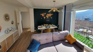 Ein modernes Wohnzimmer mit großem Fenster, einer Weltkarte an der Wand und einem Essbereich mit Tisch für zwei Personen.