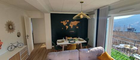 A modern living room with a large window, a world map on the wall, and a dining area with a table set for two.