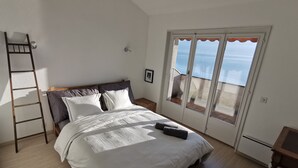 Een slaapkamer met een bed, een houten ladder, een klein tafeltje en uitzicht door een glazen deur.