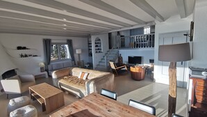 Een ruime woonkamer met een houten eettafel, banken en een open haard.