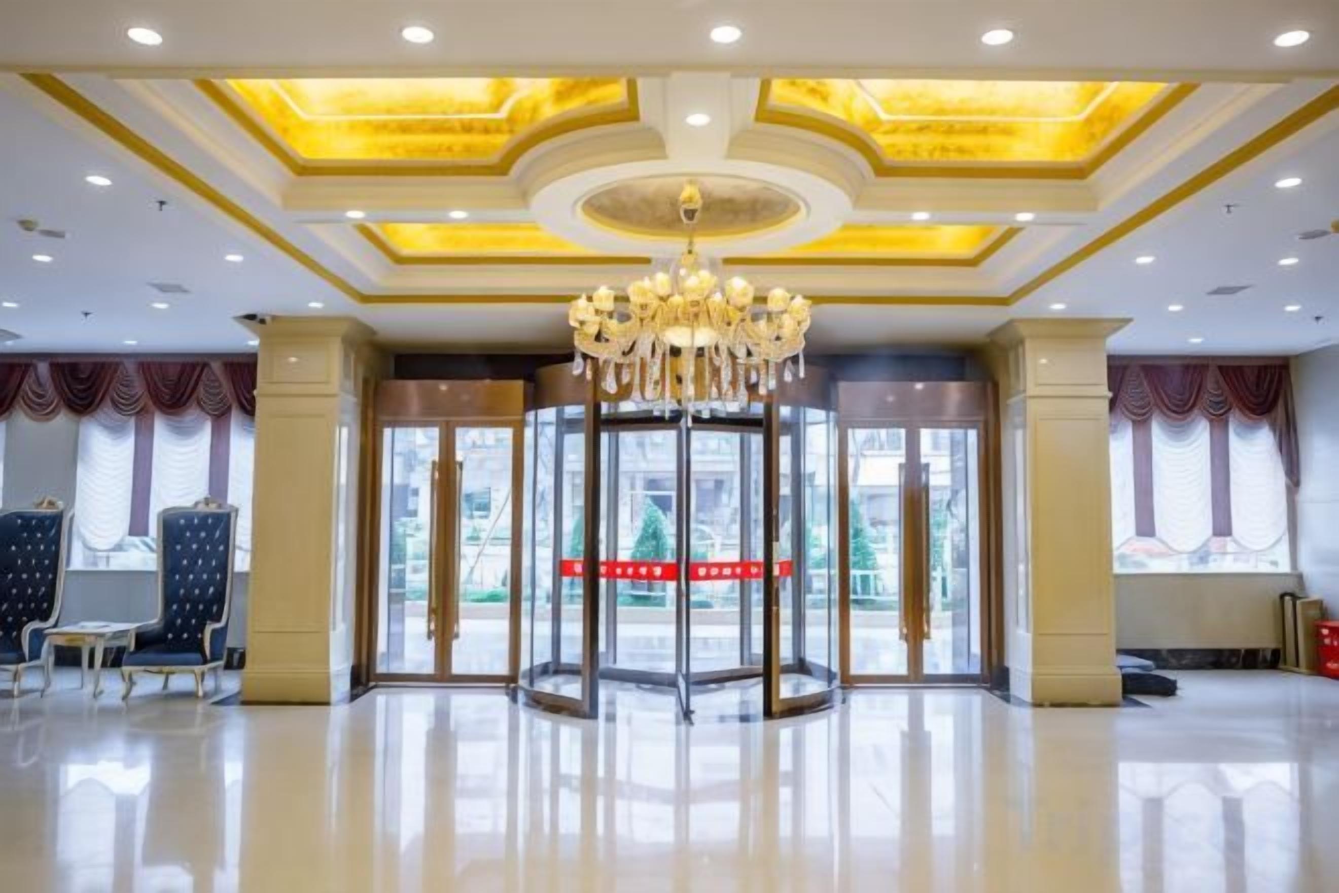 A hotel lobby with a revolving door, a chandelier, and a large window with curtains.