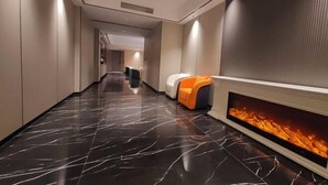 Un corredor de hotel moderno con piso de mármol negro, una zona de estar con cojines naranja y blanco, y una chimenea empotrada.