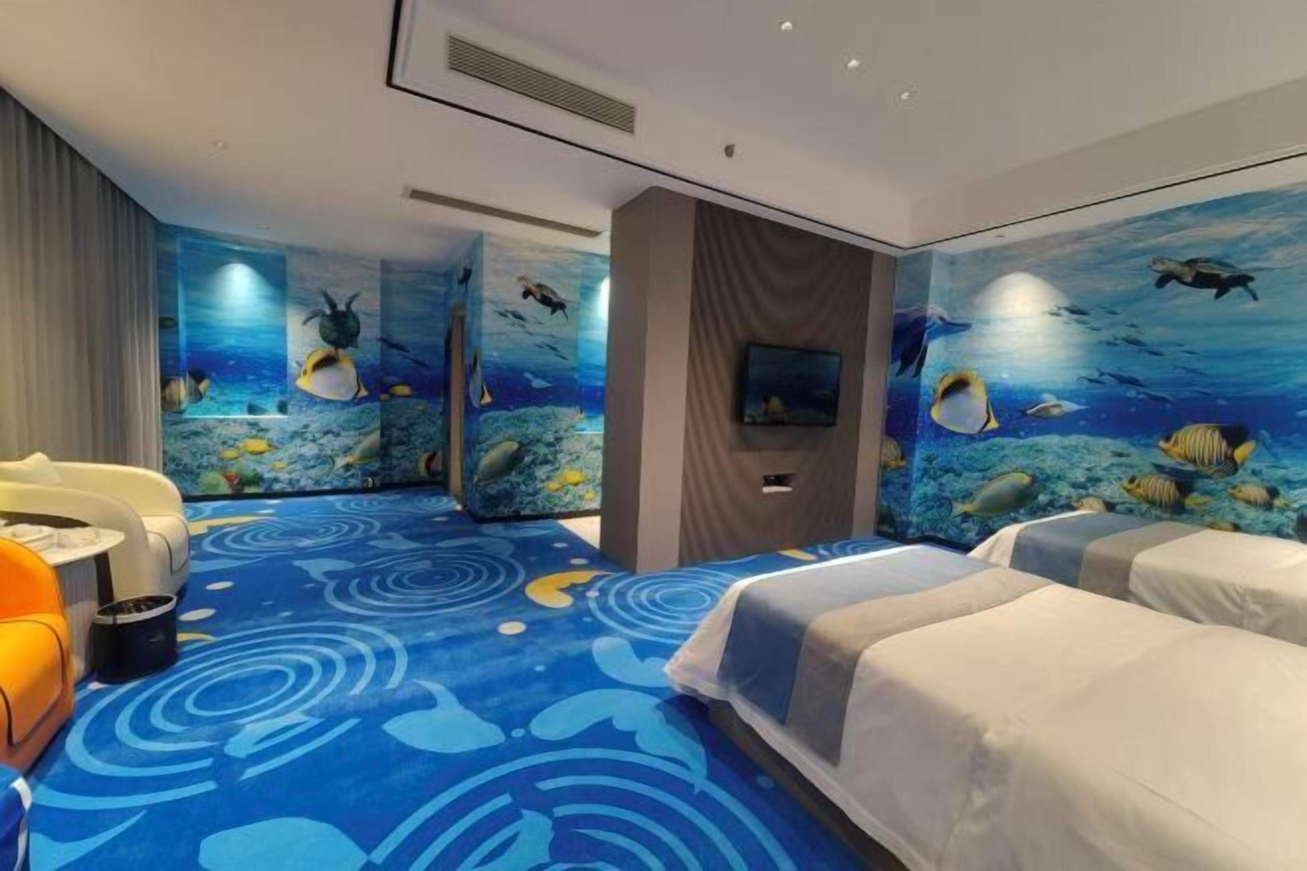 A hotel room with a large bed, two smaller beds, a sofa, and a TV. The walls are decorated with an underwater mural.