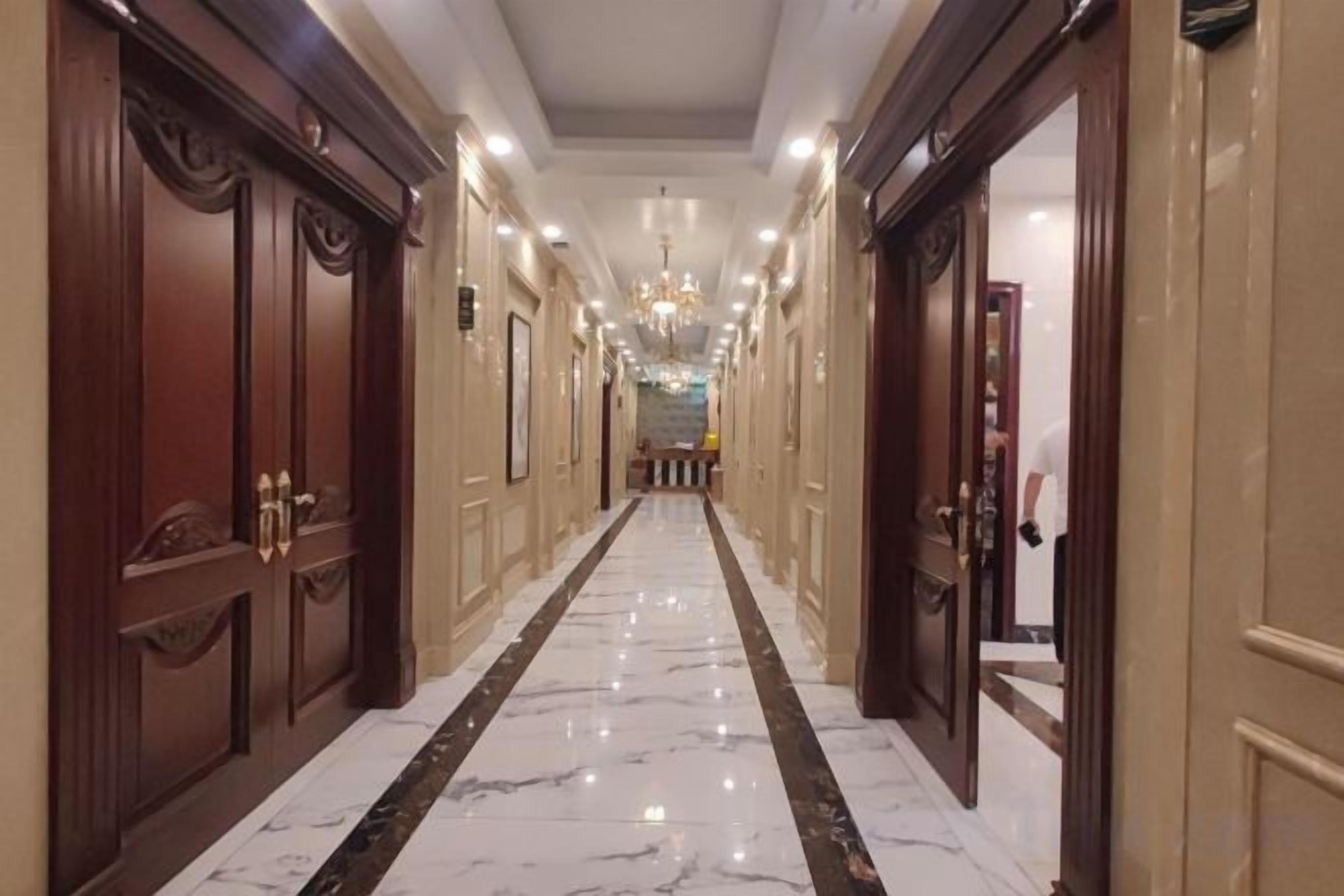 Un pasillo de hotel con puertas de madera, piso de mármol y un candelabro.