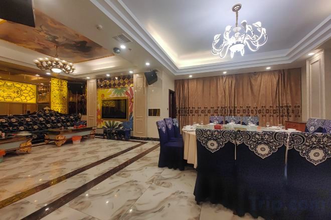 A banquet hall with a chandelier, a stage, and a long table set for a formal event.