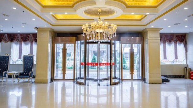 Un vestíbulo de hotel con puerta giratoria, candelabro y un gran ventanal con cortinas.
