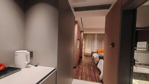 Habitación de hotel moderna con piso de madera, cama con ropa de cama naranja, mesita de noche y cafetera blanca.