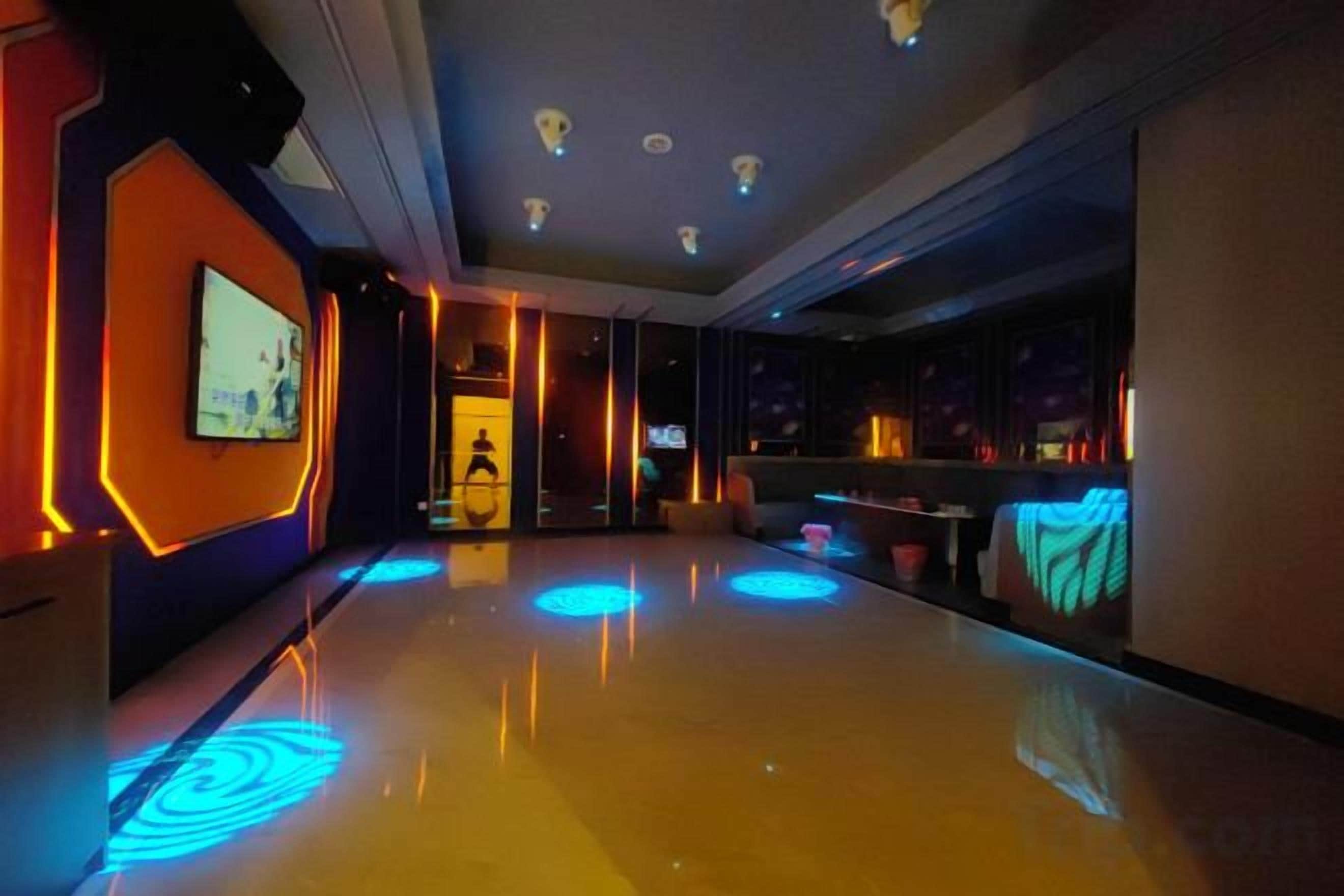 A hotel lobby with a reflective floor, a television screen, and a seating area with tables.