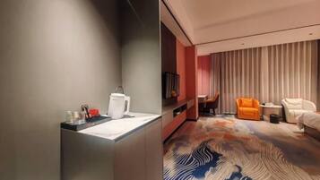 A modern hotel room with a grey wall, a white sink, a patterned carpet, an orange chair, and a white sofa.