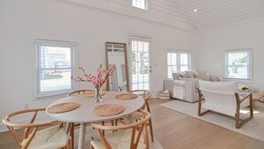 A spacious living room with a dining area, featuring a round table with chairs, a sofa, and a large mirror. - The Beach Nest-Lux Cottage Steps to the Beach (Clinton)