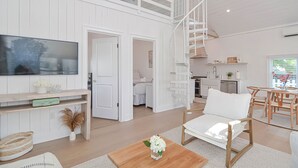 A spacious living area with a large flat-screen TV, a wooden coffee table, and a white sofa. - The Beach Nest-Lux Cottage Steps to the Beach (Clinton)