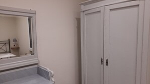 Een kamer met een witte kast, een spiegel en een klein nachtkastje met een lamp.