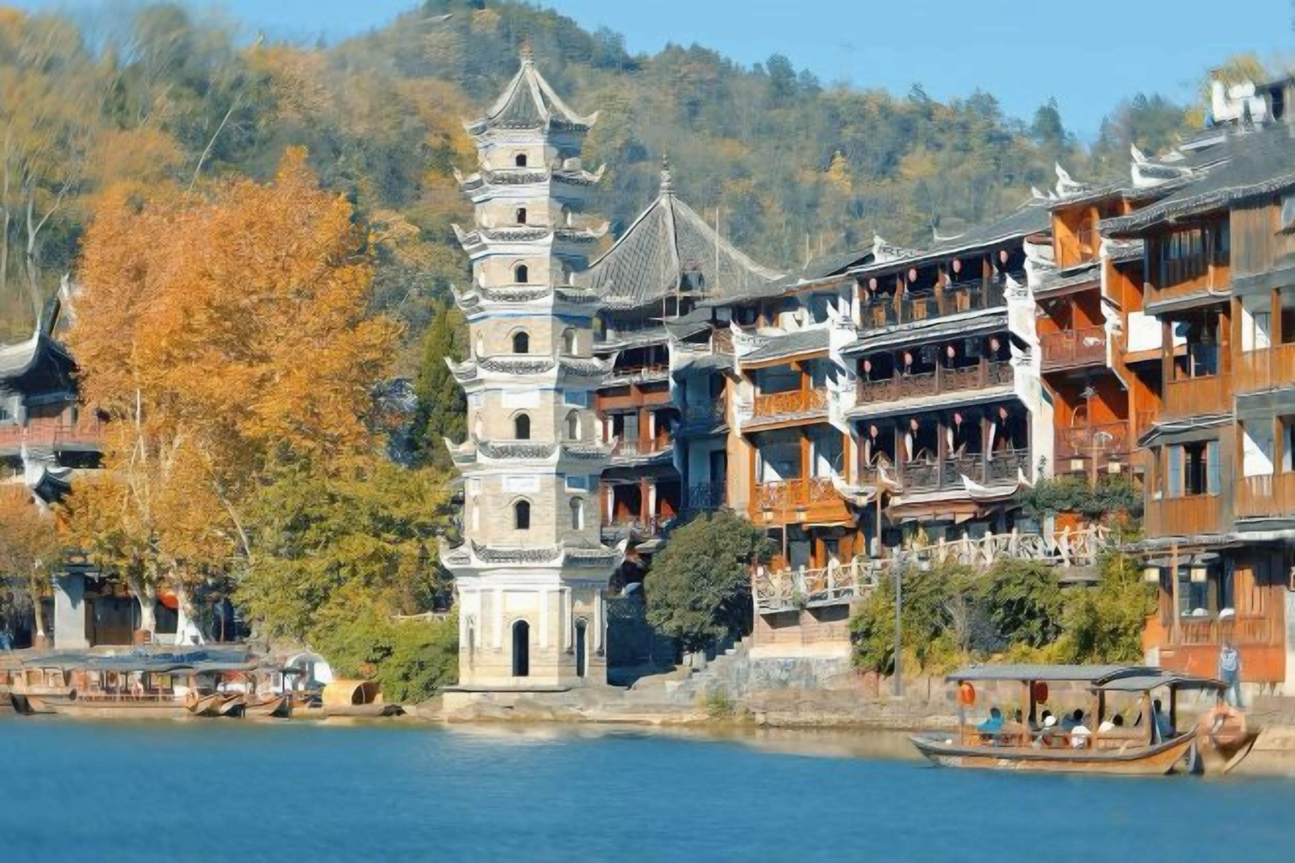 Un edificio tradicional de varios pisos con una torre destacada, ubicado junto a una masa de agua, rodeado de árboles y otras construcciones.