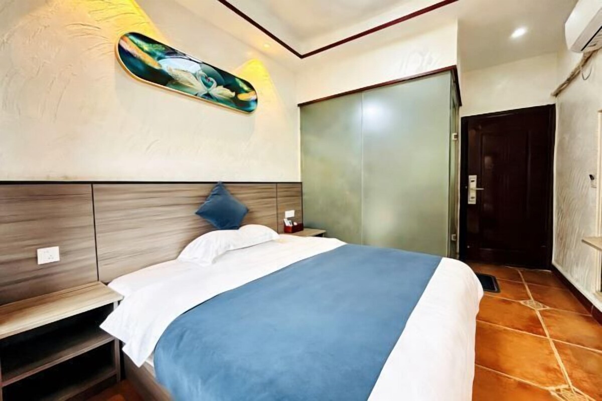 A bedroom with a bed, bedside tables, a nightstand, a wall-mounted artwork, and a sliding door.