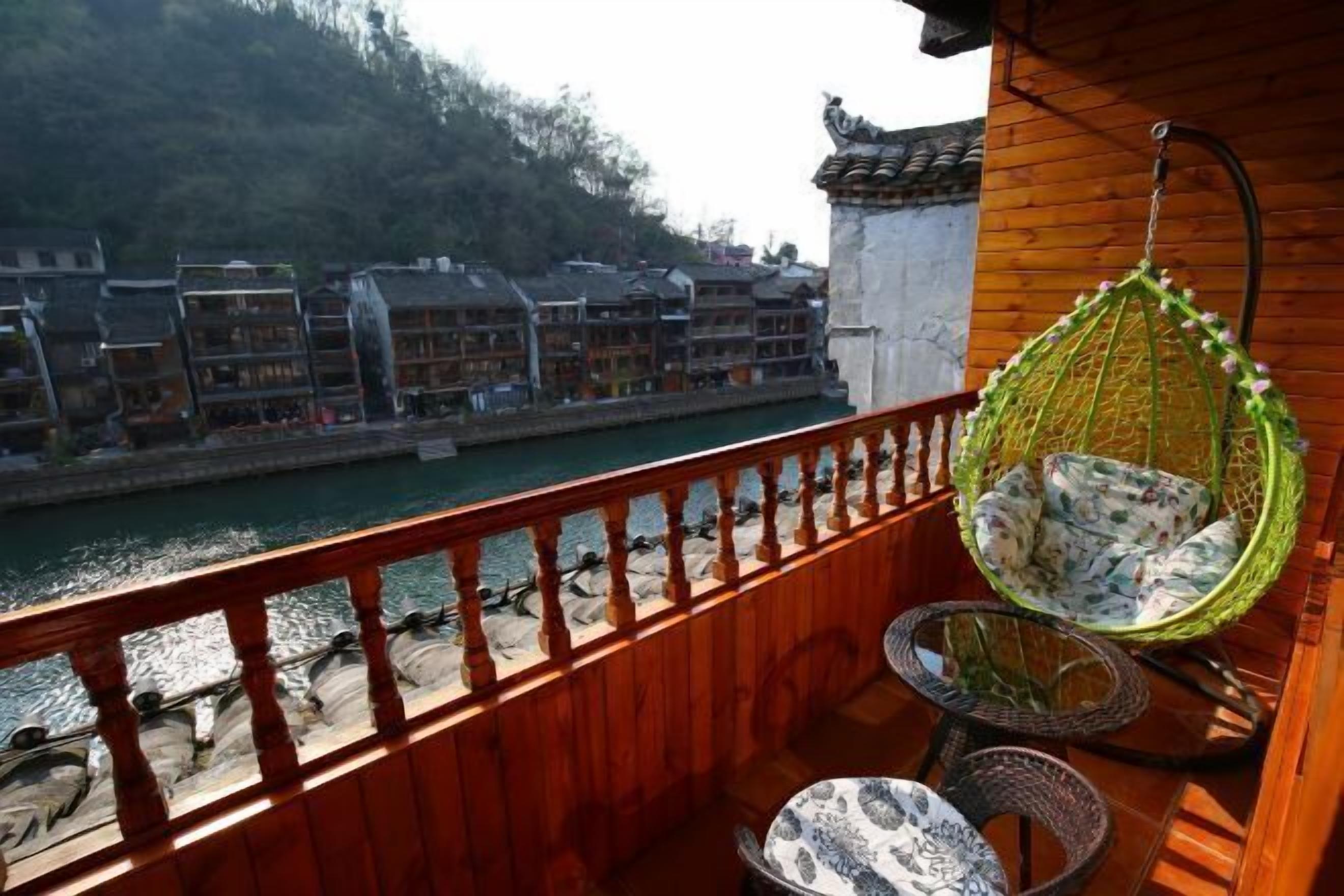 Un balcone in legno con una sedia a dondolo, un tavolo rotondo e vista su edifici tradizionali lungo un fiume.