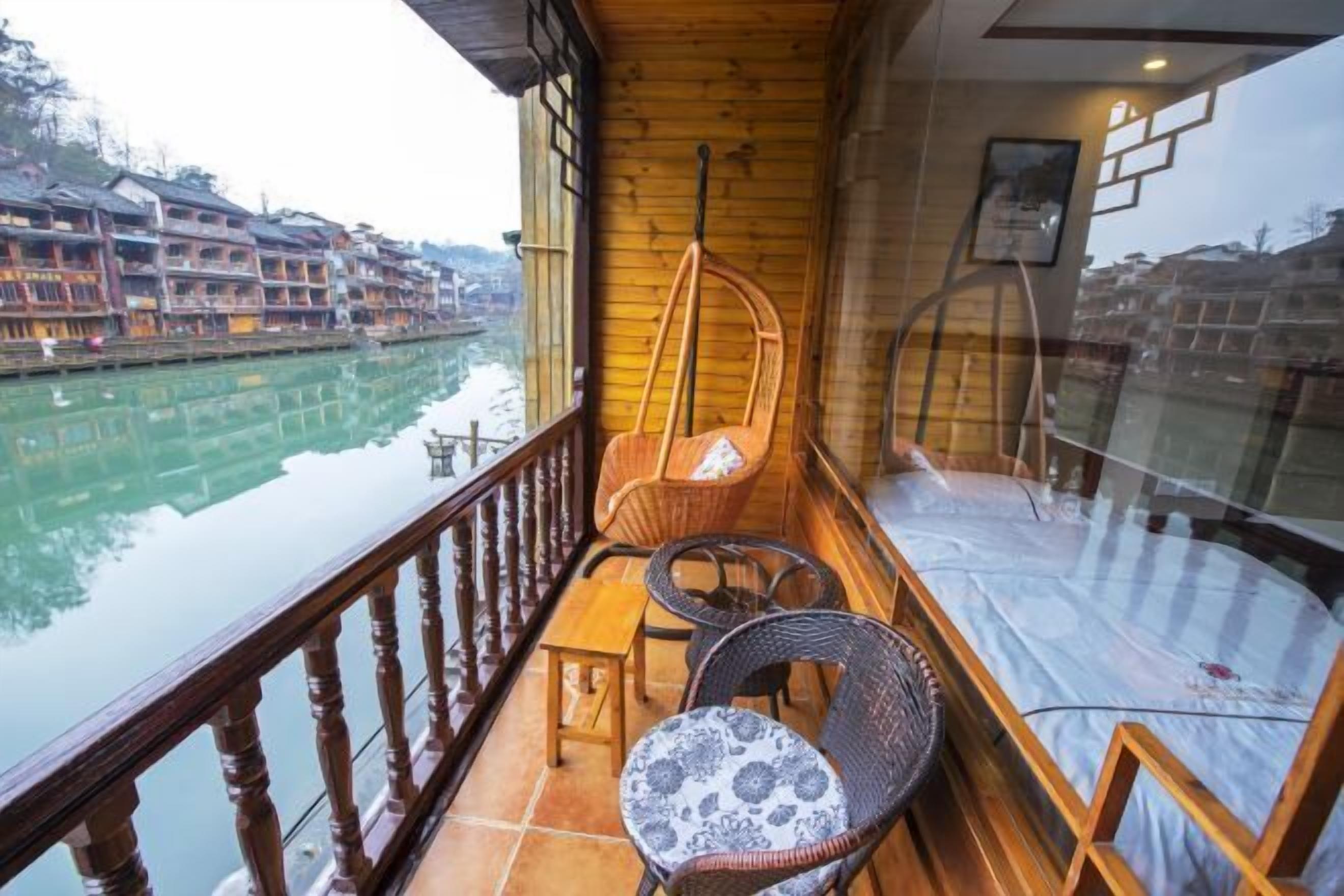 A balcony with wicker furniture, a view of a river, and traditional buildings in the background.