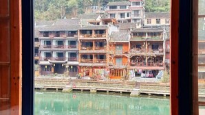 Un edificio tradicional de varios pisos con balcones, un puente de madera y una masa de agua al frente.