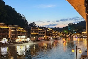 A riverside view of traditional buildings with reflective water, a bridge, and a row of illuminated windows. - Fenghuang Memory River View Inn - Near Ancient City & River View Balcony (Fenghuang County)
