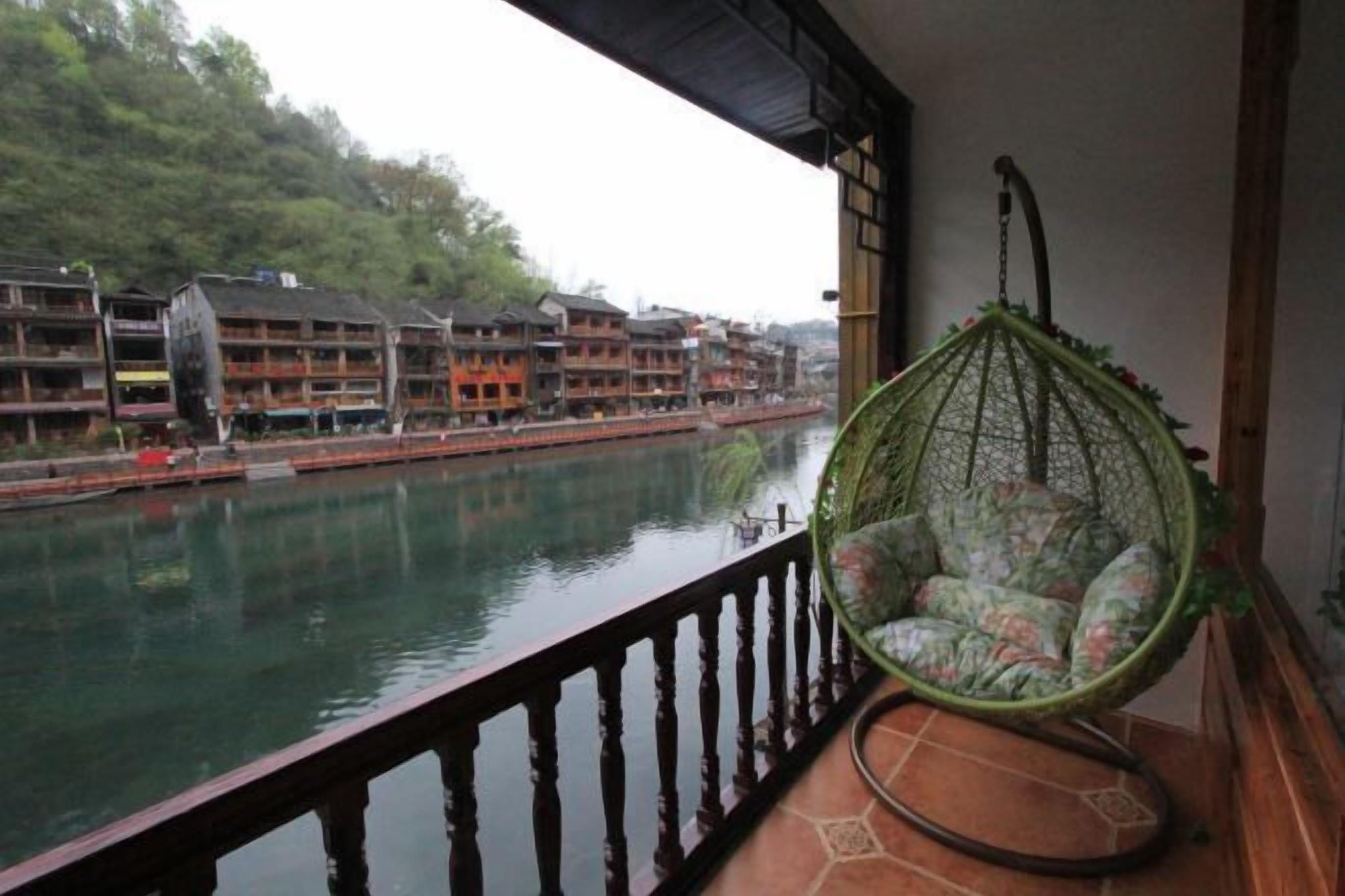 A balcony with a wicker chair overlooking a river with traditional buildings in the background.