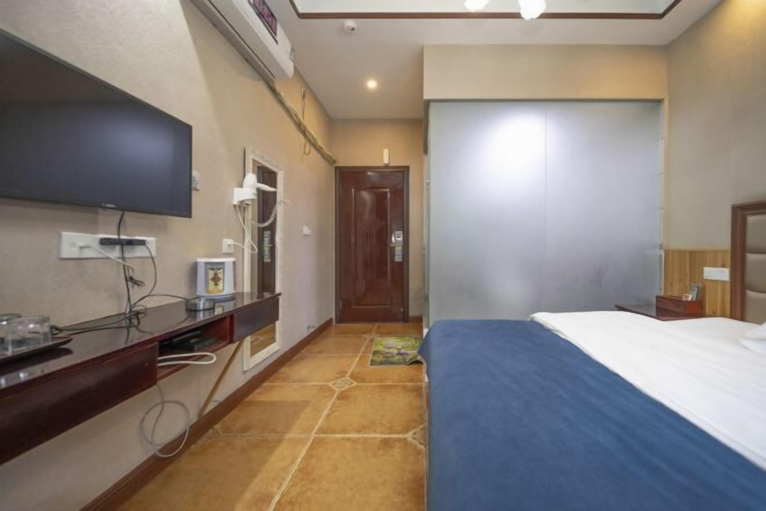 A hotel room with a bed, a desk with a flat-screen TV, a door, and a tiled floor.