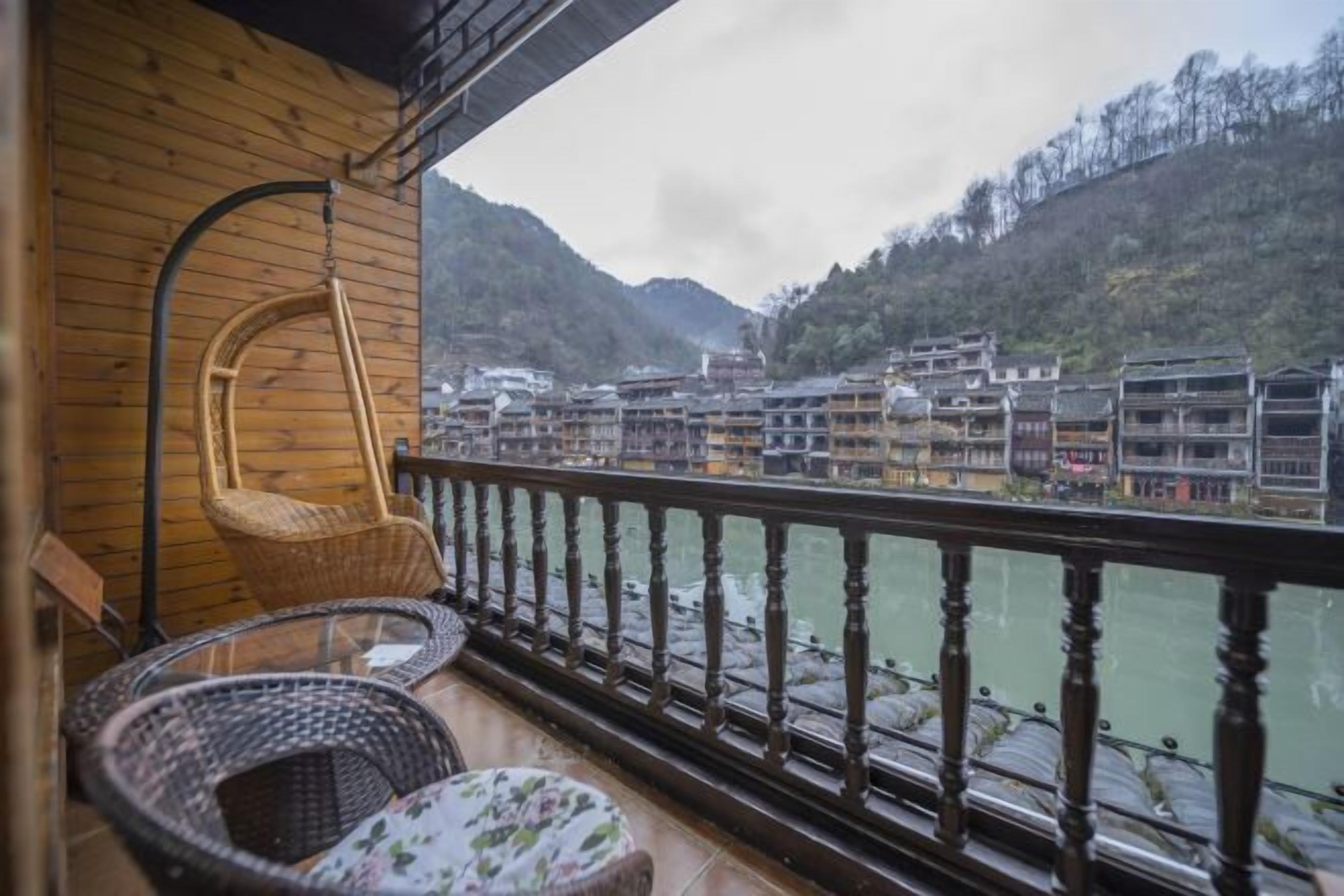 A balcony with wicker furniture overlooking a river and traditional buildings.