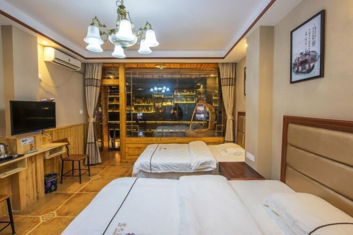 A hotel room with two beds, a desk with a TV, and a large window with curtains.