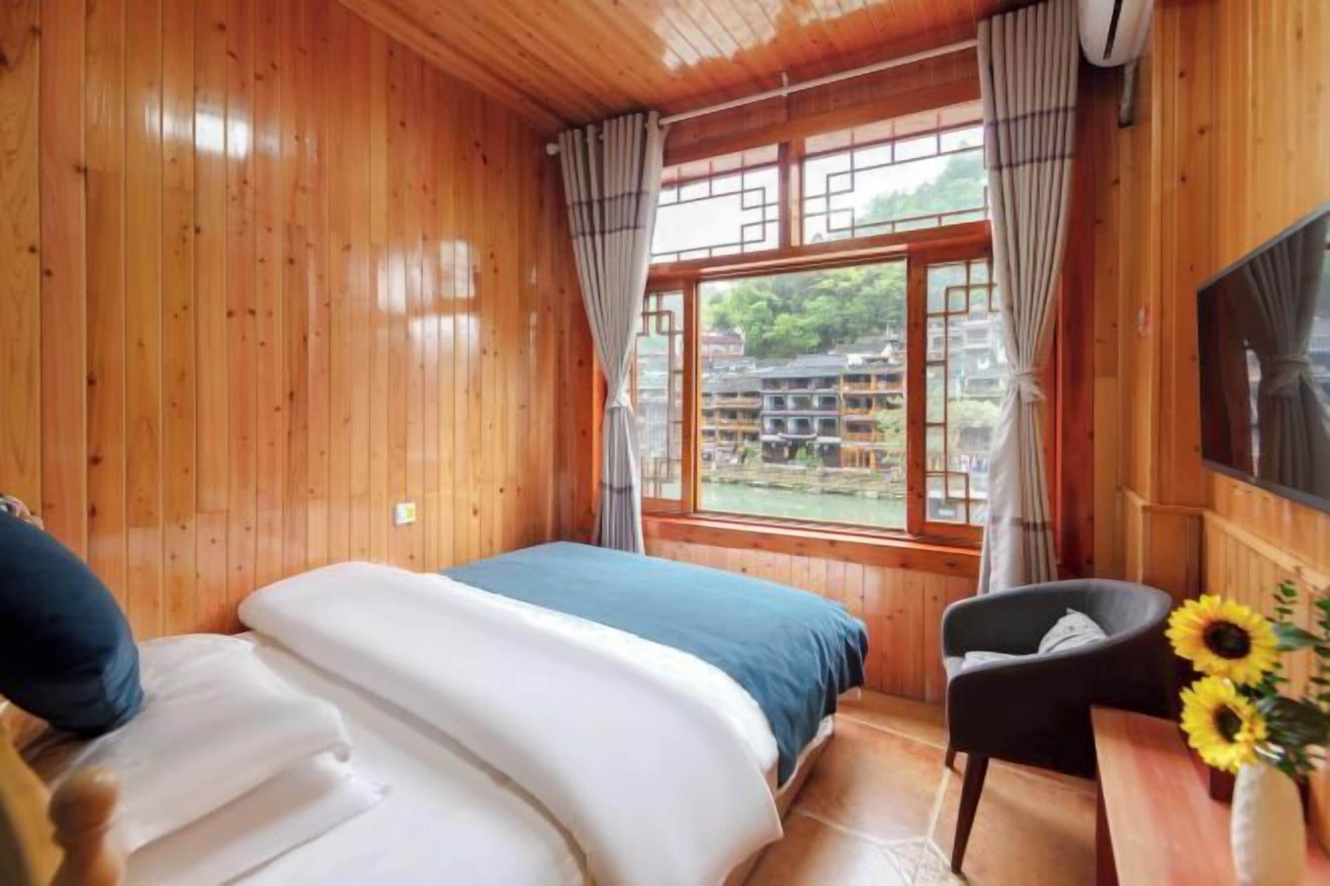 A wooden room with a bed, a chair, and a window with curtains.