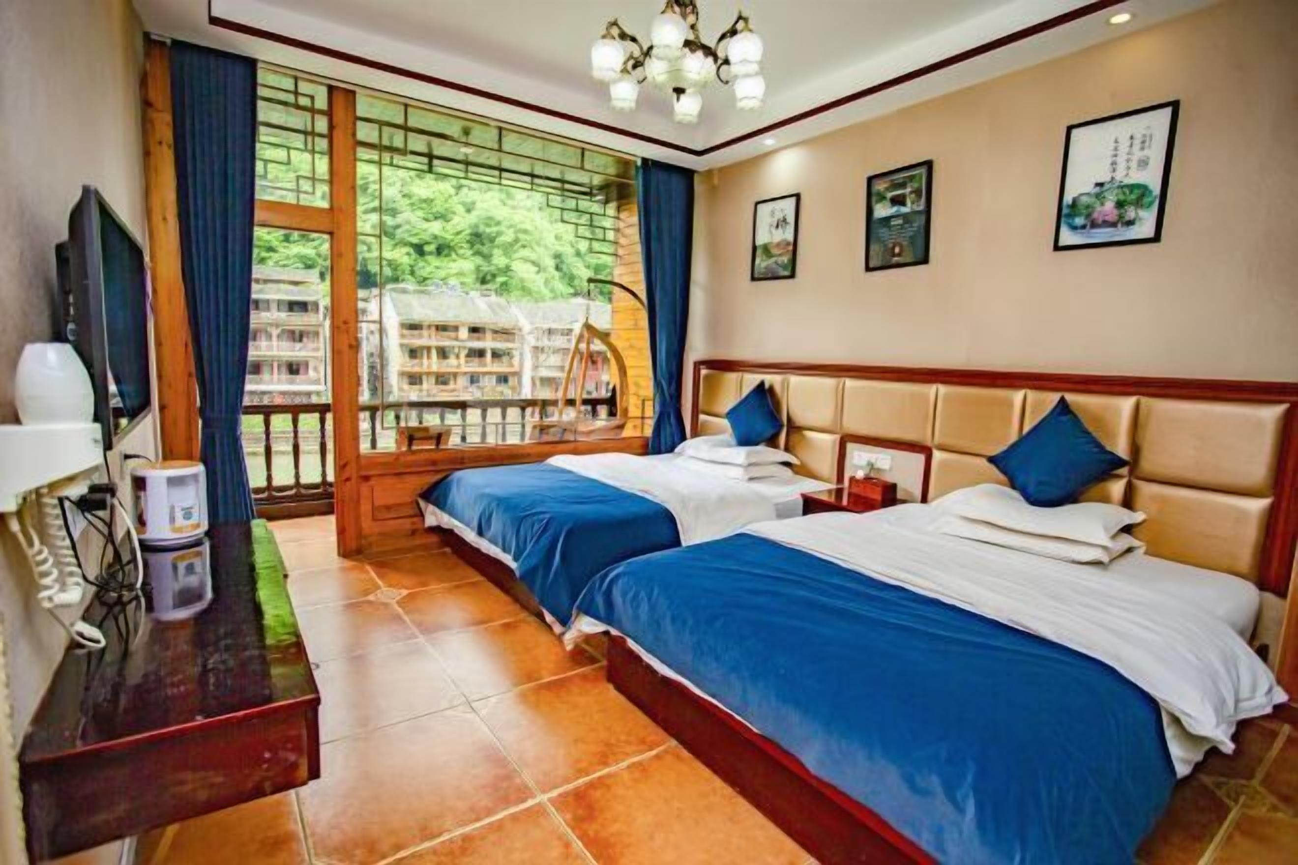 Une chambre d’hôtel avec deux lits, une télévision, un bureau avec un téléphone et une vue sur la verdure grâce à de grandes fenêtres.