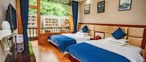Une chambre d’hôtel avec deux lits, une télévision, un bureau avec un téléphone et une vue sur la verdure grâce à de grandes fenêtres.