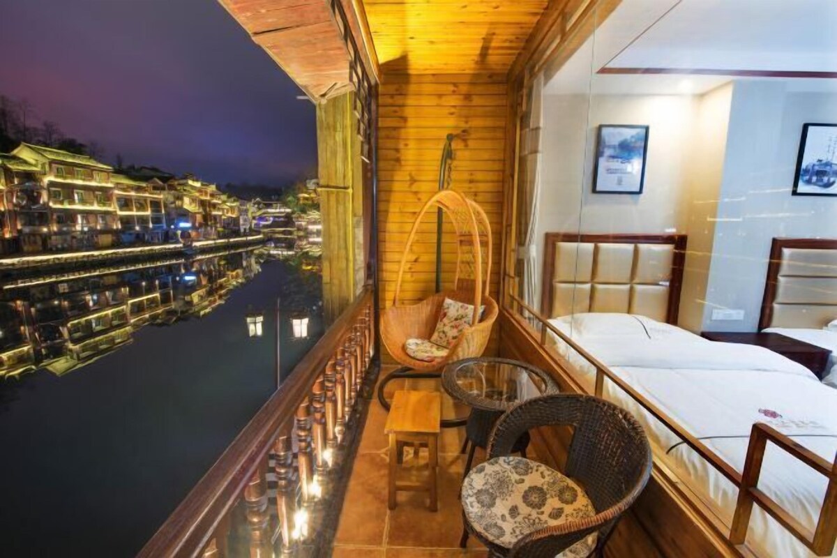 A balcony with wicker furniture, a bed, and a view of a water canal with buildings.