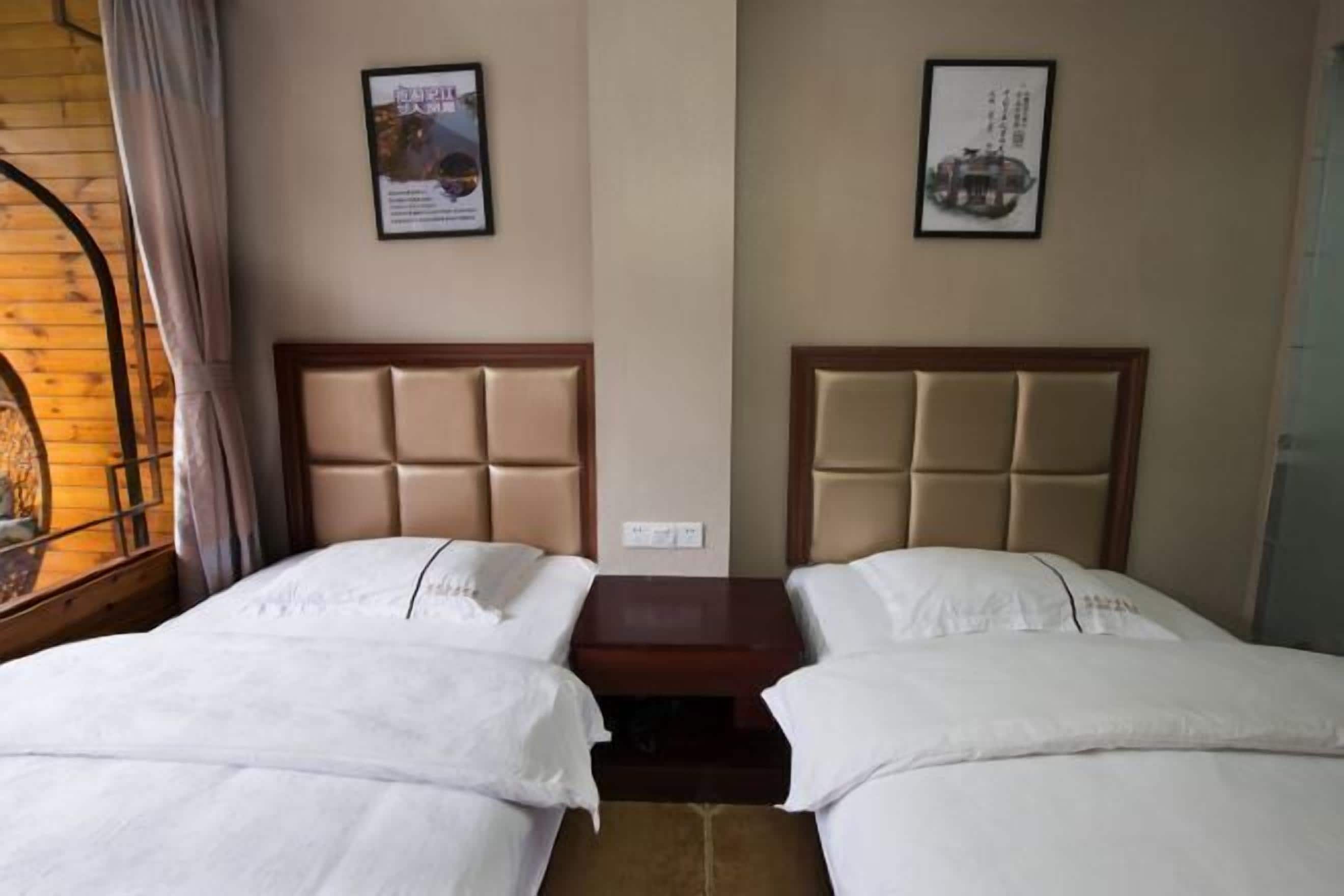 Een hotelkamer met twee bedden, een houten hoofdeinde en een raam met gordijnen.