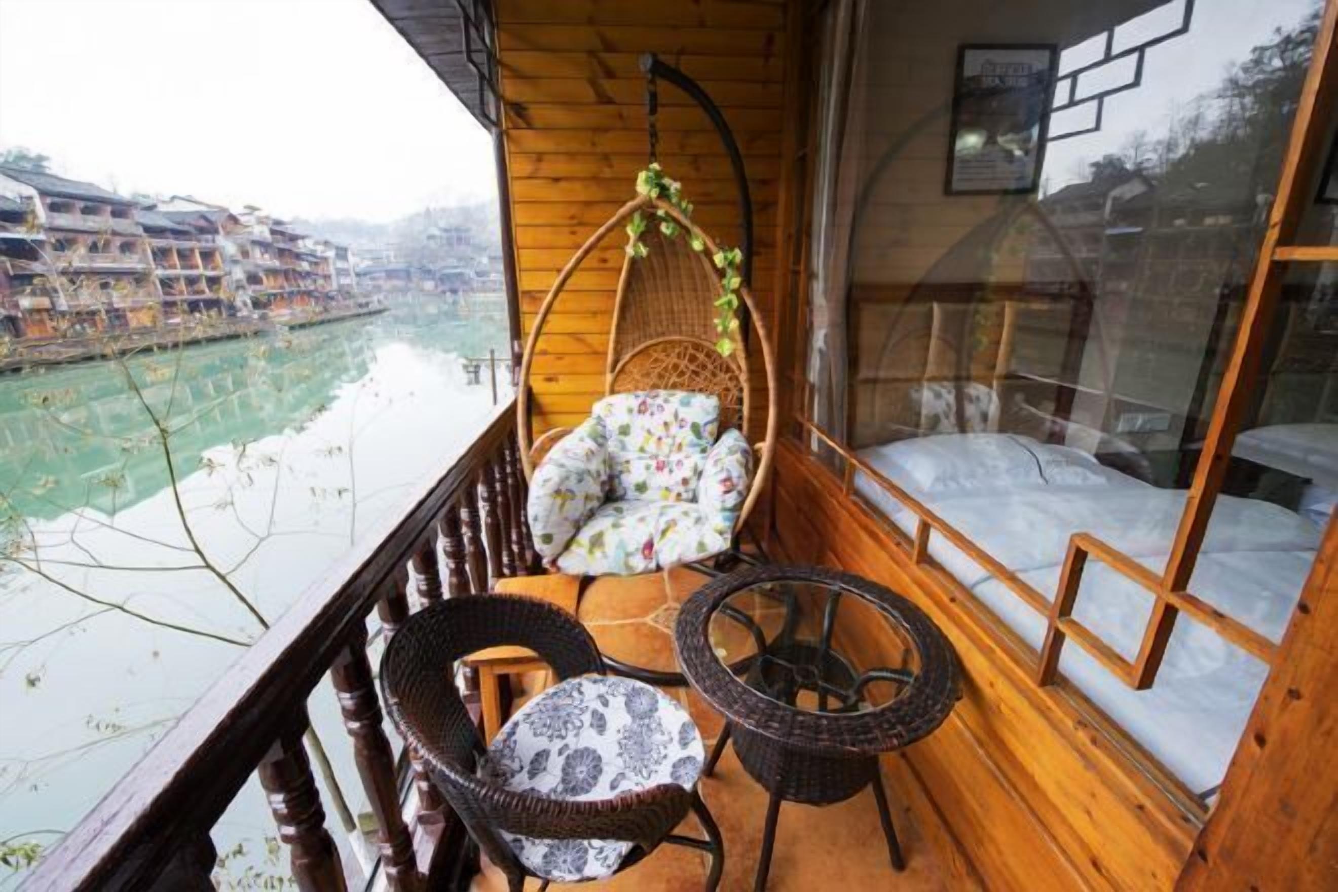 Un balcon en bois avec un fauteuil suspendu, une petite table et un lit doté d’une tête de lit à motifs géométriques.