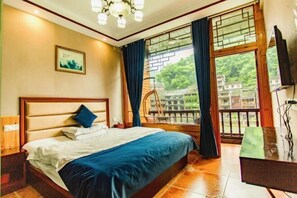 A bedroom with a large bed, a wooden headboard, a nightstand, a TV, and a balcony with a view of greenery. - Fenghuang Memory River View Inn - Near Ancient City & River View Balcony (Fenghuang County)