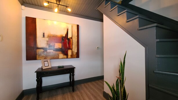 Un couloir orné d’un grand tableau abstrait, un banc en bois avec une plaque commémorative et un escalier.